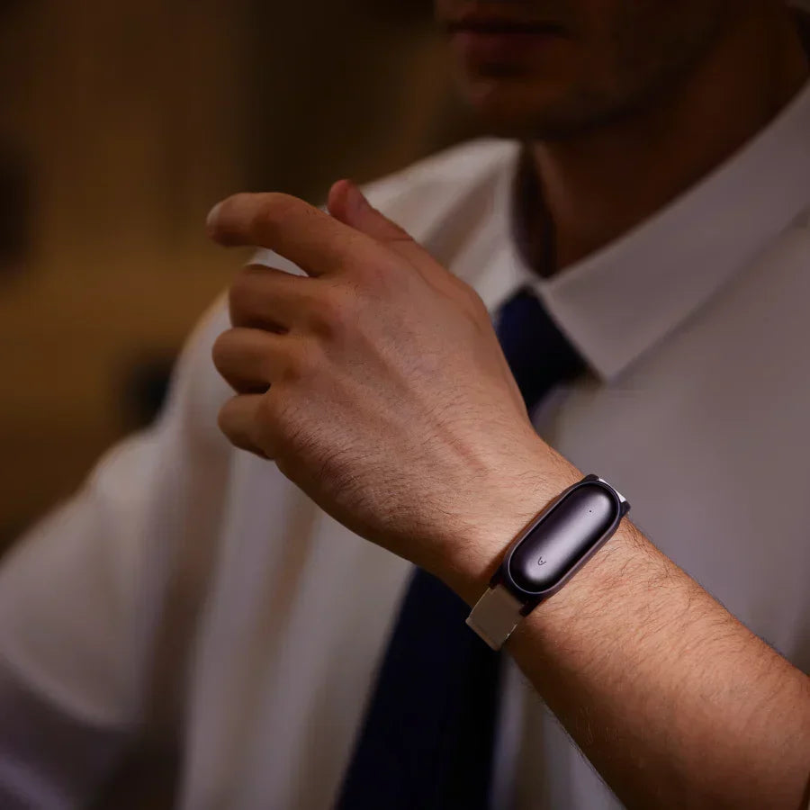 A black Plaud NotePin worn on a silver wristband by a professional in a white shirt and tie.