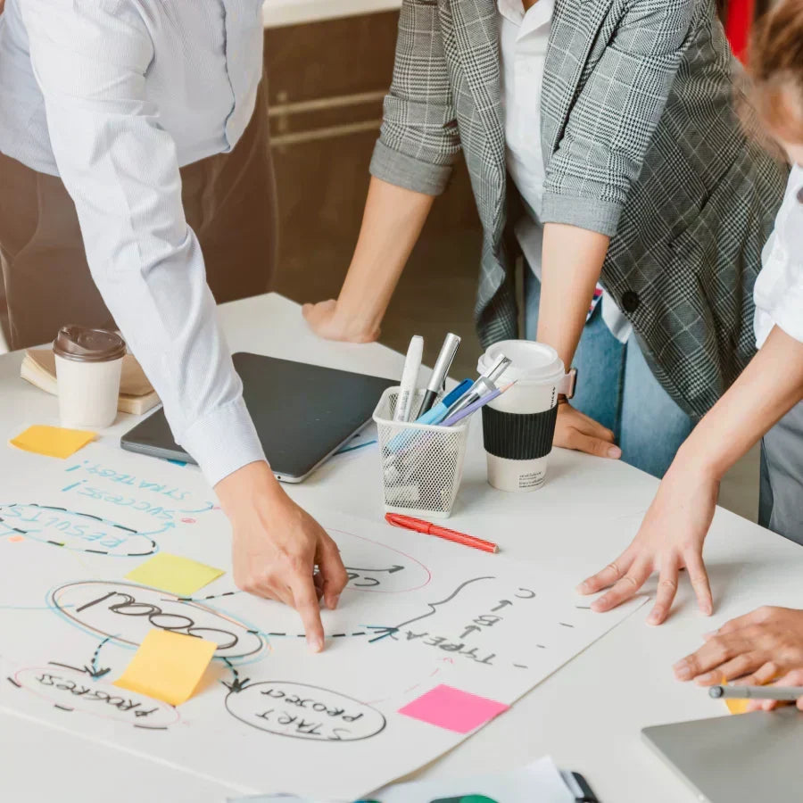Professionals brainstorming at a table; one wears a silver Plaud NotePin on a wristband.