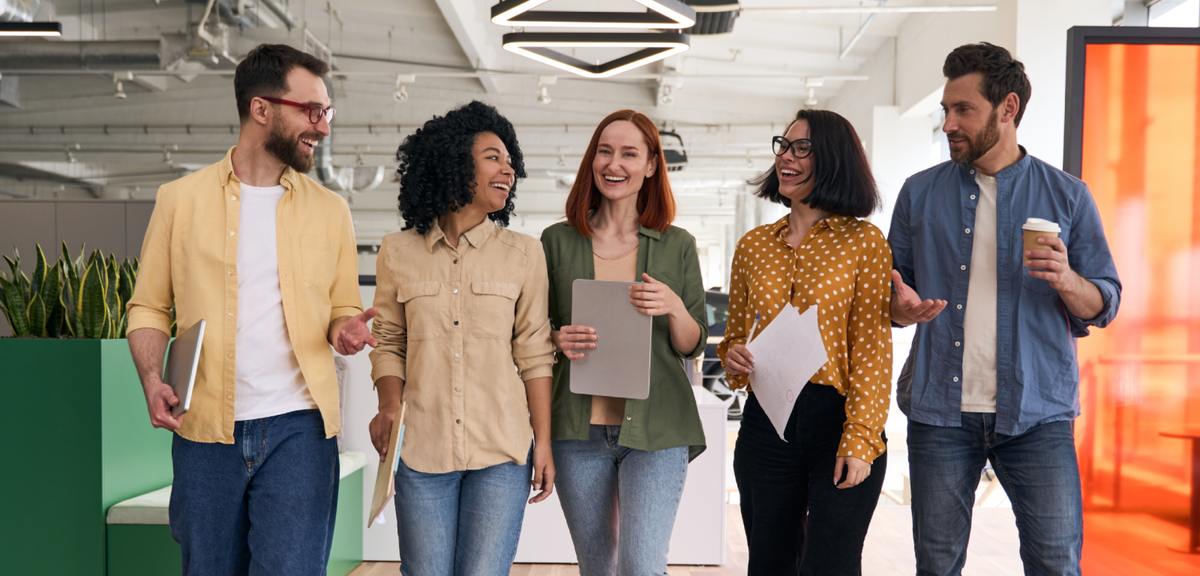 A diverse group of smiling professionals walking and talking in a modern, open-plan office.