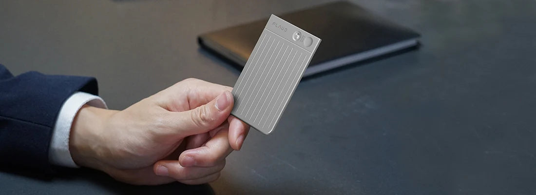 A hand holds a silver Plaud Note Pro AI voice recorder, featuring a ribbed texture and a small display screen.