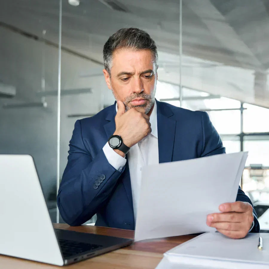 Businessman in a blue suit reviewing documents while wearing a silver Plaud NotePin.