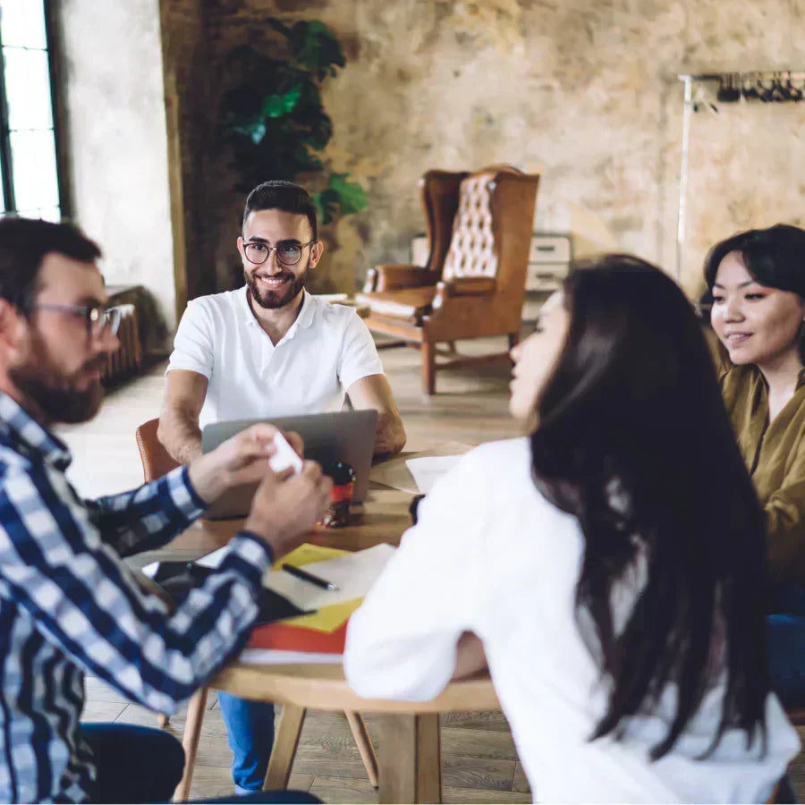 Four colleagues in a collaborative meeting, with one person holding a white Plaud Note AI voice recorder.