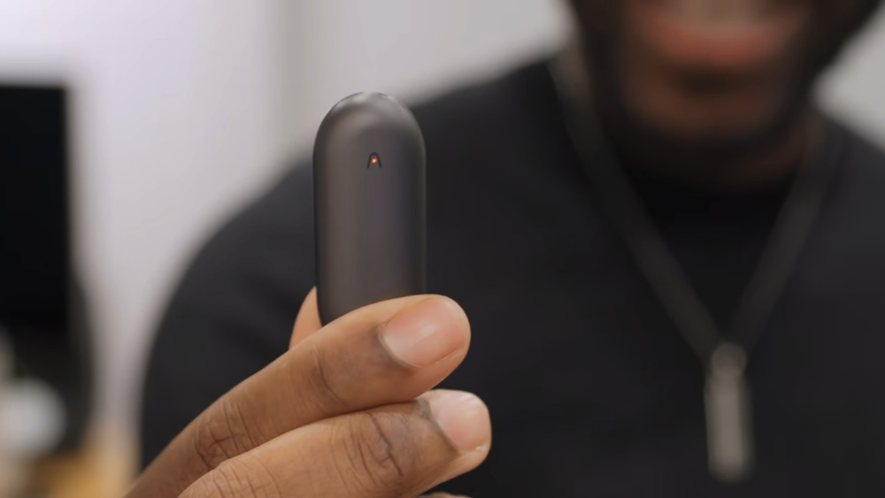A person holding a Cosmic Gray Plaud NotePin wearable AI voice recorder with a red indicator light.