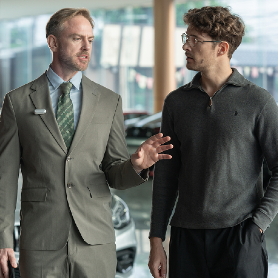 A professional wearing a silver Plaud NotePin on his lapel while talking to a client in a showroom.