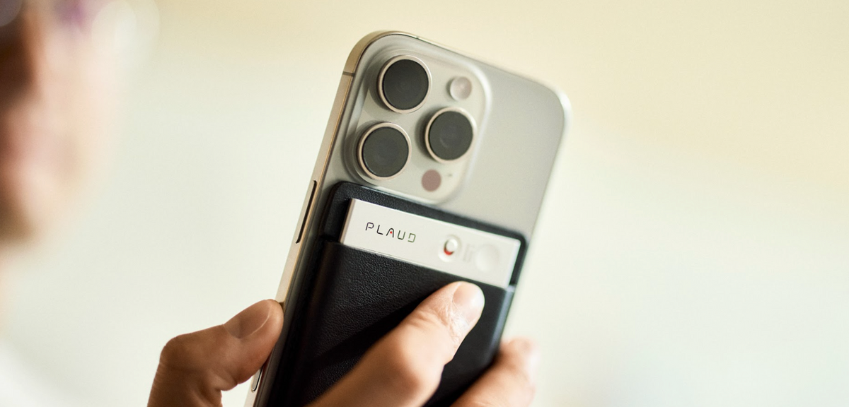 Silver Plaud Note in a black case attached to an iPhone, with a user pressing the recording button.