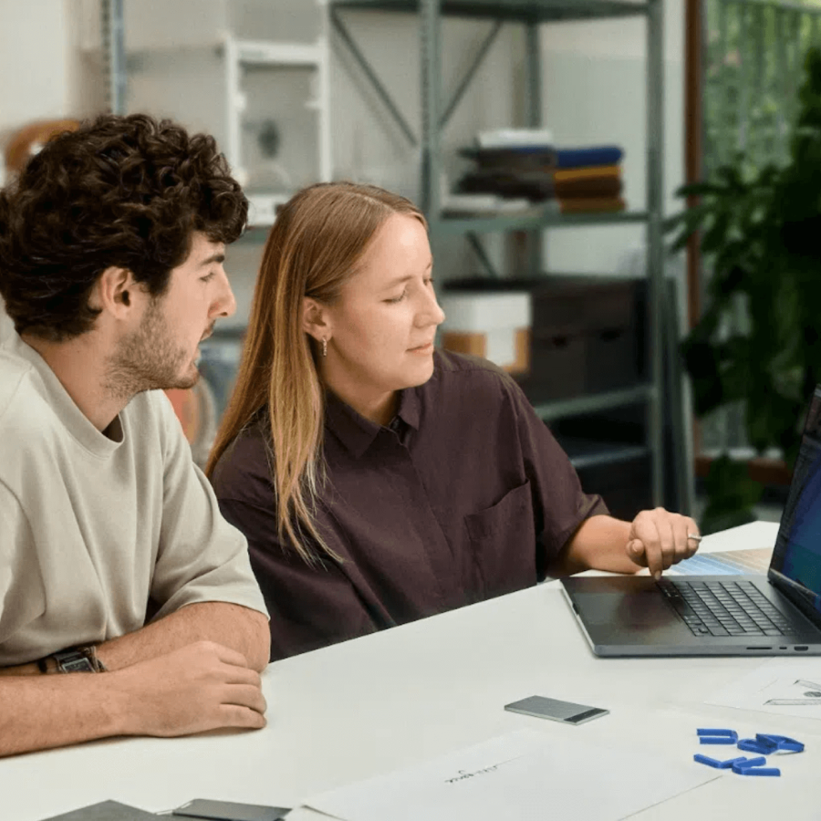 Two colleagues collaborating at a desk with a laptop and a silver Plaud Note.