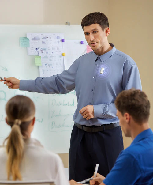 A man wearing a silver Plaud NotePin on his shirt while presenting at a whiteboard during a meeting.