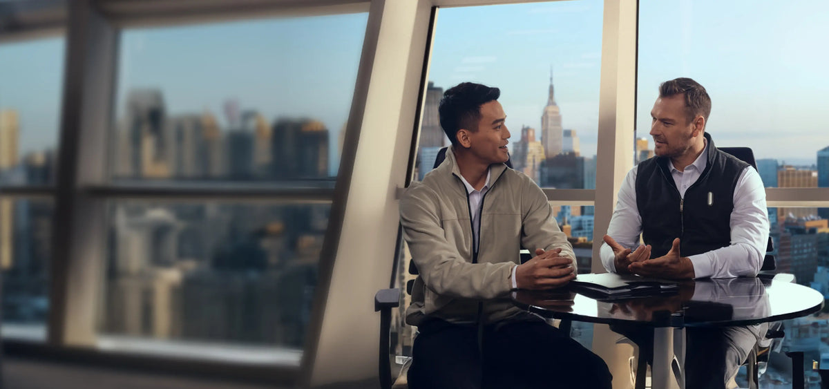 Two men meeting in a city office; one wears a white Plaud NotePin on his vest.