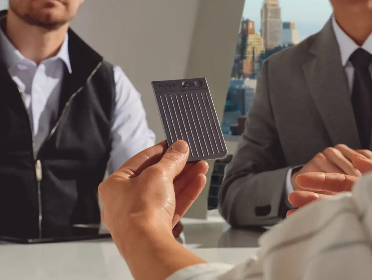 A person holds a gray Plaud Note Pro AI voice recorder during a professional meeting in an office.