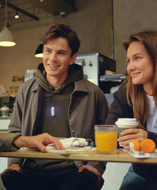 A man wearing a silver Plaud NotePin on a lanyard during a conversation at a cafe.