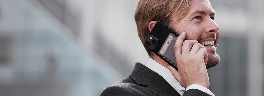 Man talking on a phone with a silver Plaud Note attached to the back.