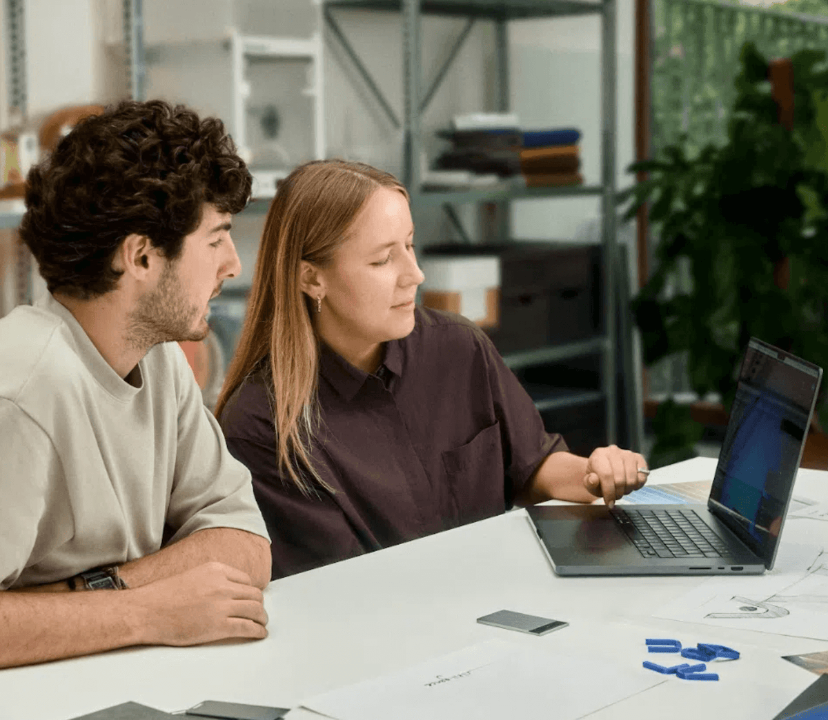 Two colleagues review data on a laptop with a silver Plaud Note on the desk.